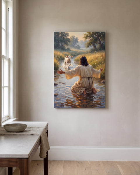 Vertical canvas of a lamb running through a stream toward Jesus kneeling with open arms, hung on a warm greige plaster wall