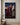 Forgiven canvas print hanging on a pale plaster wall above a low walnut console holding an olive branch in a stoneware vase