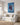 Blue oil painting of Jesus and a woman walking the shore, hung above a linen sofa in a coastal living room