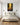 Golden forest path wall art centered over a linen headboard in a calm white bedroom