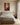 Golden light at the hem of Jesus' robe on canvas above a linen upholstered king headboard in a sunlit primary bedroom