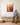 Grandfather holding a wooden toy sailboat looks up at the boy version of the canvas in his grandchildren's playroom