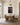 On the panelled end wall of a dining room above a solid oak table with cane-back chairs and a brass and alabaster pendant
