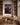 On the plaster wall between built-in oak bookcases in a study, an oak desk with a cognac leather chair and an open book below