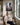 Woman with a coffee mug and open Bible sitting in a sunroom armchair beneath the canvas of Christ's nail-scarred hand reaching out
