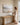 Woman pausing while arranging eucalyptus to look at a Be Still and Know landscape canvas in a sunlit room