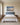 Footprints in the Sand painting-style canvas over a blue upholstered headboard in a sunlit primary bedroom