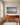 Painting-style canvas of a beach at dawn with one set of footprints above a cherry sideboard in a morning room