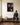 Man in a charcoal sweater sitting on a hall bench looks up at a canvas of Jesus crowned with thorns