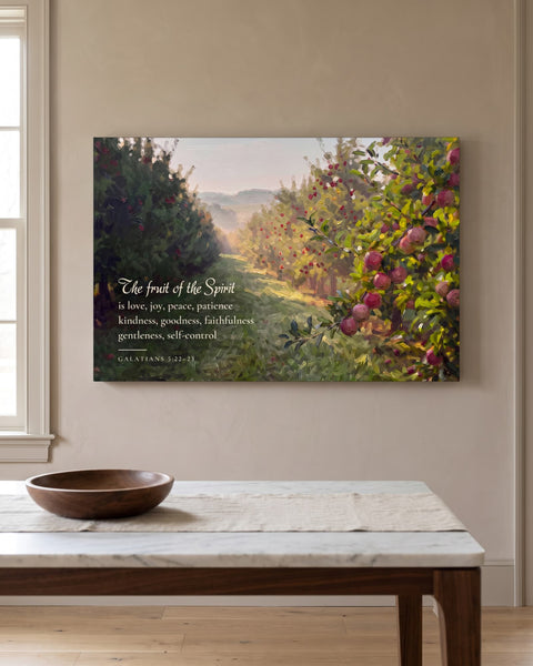 Painting-style apple orchard canvas with the Galatians 5:22-23 fruit of the Spirit verse, front view on a taupe plaster wall above a marble-topped console