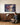 A man kneeling to stack firewood looks up at the canvas of Jesus holding a man in the storm above a walnut sideboard