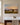 Painting-style sunrise meadow canvas with Lamentations 3:22-23 hanging on a greige plaster wall above a marble-topped console