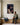 Man in a work shirt sitting on a hall bench looks up at a canvas of Jesus crowned with thorns
