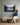 Woman seated on an oak bench with an open Bible looking up at a Psalm 121 lake canvas on a sage panelled wall
