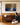A woman kneeling on an oak floor beside a walnut sideboard, looking up at the Gethsemane canvas on the wall above her