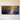 Extra-wide panoramic canvas of Jesus kneeling in prayer under a golden tree, centered on a warm cream plaster wall above a pale oak table