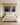 Indigo and gold panoramic canvas above an ivory upholstered bed set against a pale oak panelled wall