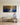 A man in a blue shirt seated on a long oak bench, looking up at the panoramic Gethsemane canvas on a panelled wall