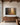 Painting-style Proverbs 3:5-6 forest path canvas hanging above a walnut credenza in a home office with a steel-framed window