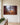 Nativity canvas with the shadow of a cross on a stone stable wall, hung on an ivory plaster wall beside a console dressed with fresh cedar
