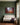 Christmas nativity wall art on a moss-green panelled wall above a linen settee with a tartan blanket and wrapped gifts