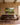 Large 48x32 painting-style canvas of a stream through green pasture with Psalm 23 lettering above a long brown linen sofa in a camel paneled den