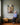 Grandmother seated on an oak bench looking up at the vertical canvas of a lamb running to Jesus through water