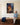 Woman in a chambray shirt sitting on a hall bench looks up at a canvas of Jesus finding the lost lamb in the rain